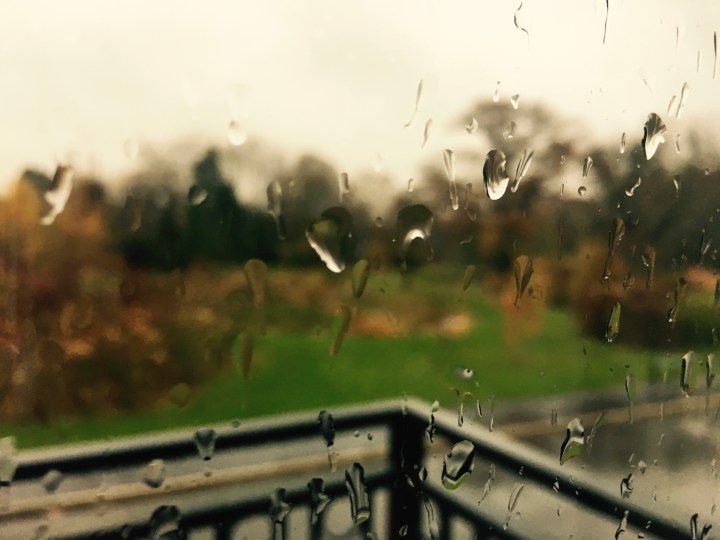 Raindrops on a balcony window overlooking an autumnal landscape
