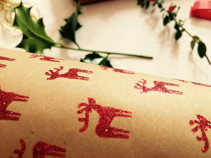 Christmas wrapping paper with holly, ribbons and gold ties in the background