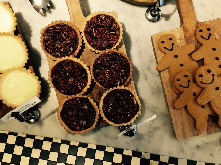 Lemon tarts, pecan tarts and gingerbread displayed on wooden boards on marble table sitting on a black and white checkered tile floor