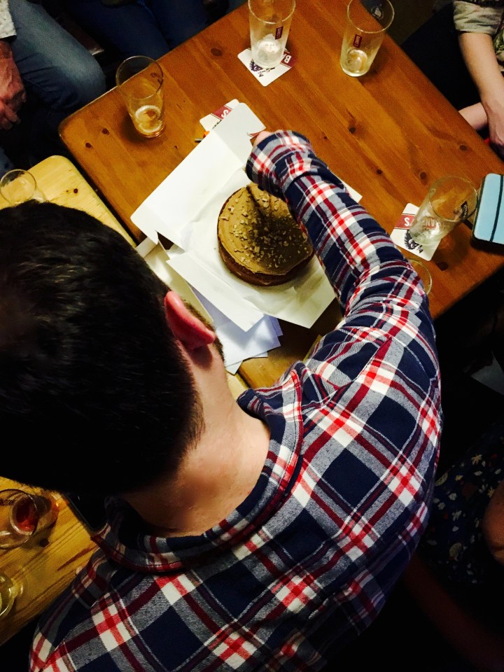 Aerial shot of man cutting a birthday cake at a pub surrounded by friends.