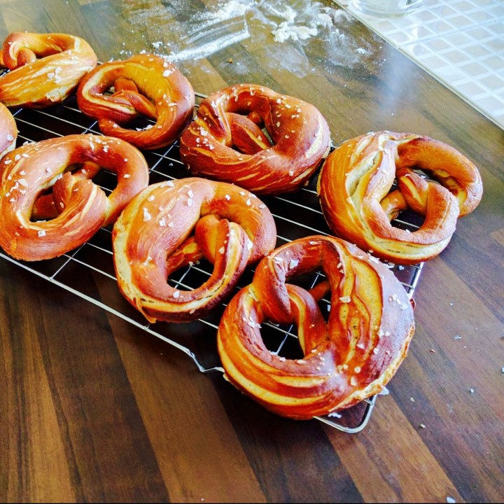 Rows of home made pretzels sitting on a cooling rack on a kitchen bench.