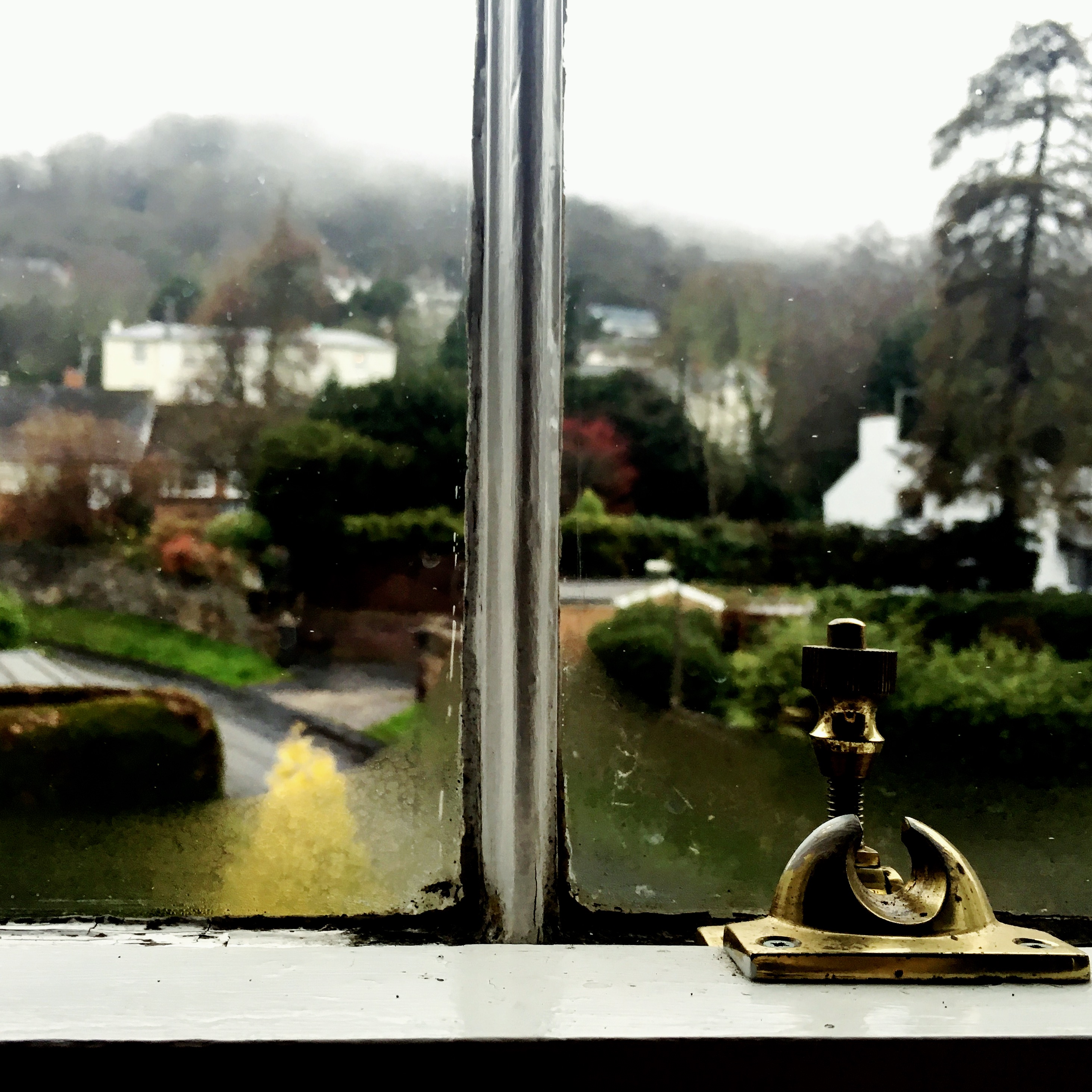 Looking out of a sash window in a Victorian era house onto a rainy day with clouds covering nearby hills.
