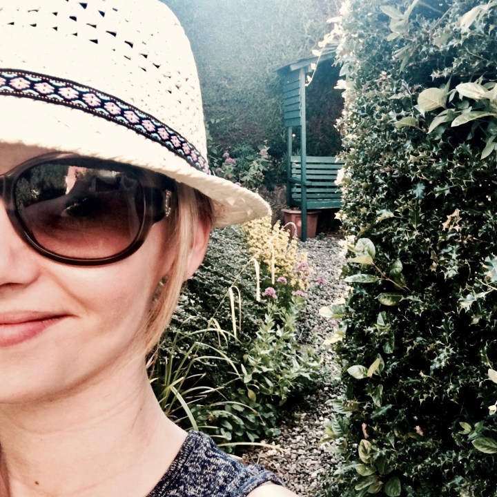 Woman in straw hat and sunglasses standing in an English cottage garden.