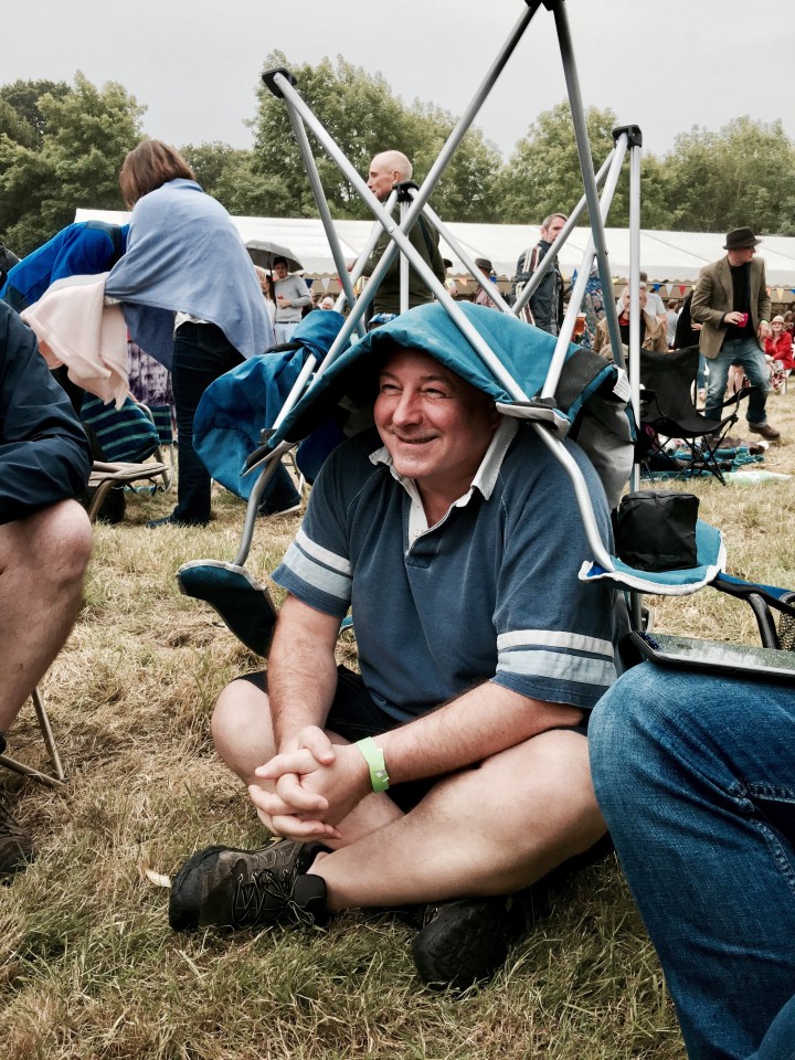 Man wearing camp chair on head to prevent getting wet in a shower of rain.