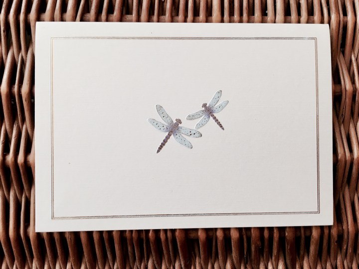 Dragonfly greeting card sitting atop a wicker picnic basket.