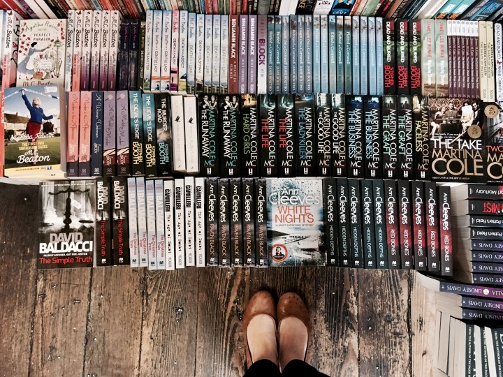 Feet on wooden floorboards surrounded by dozens of books.