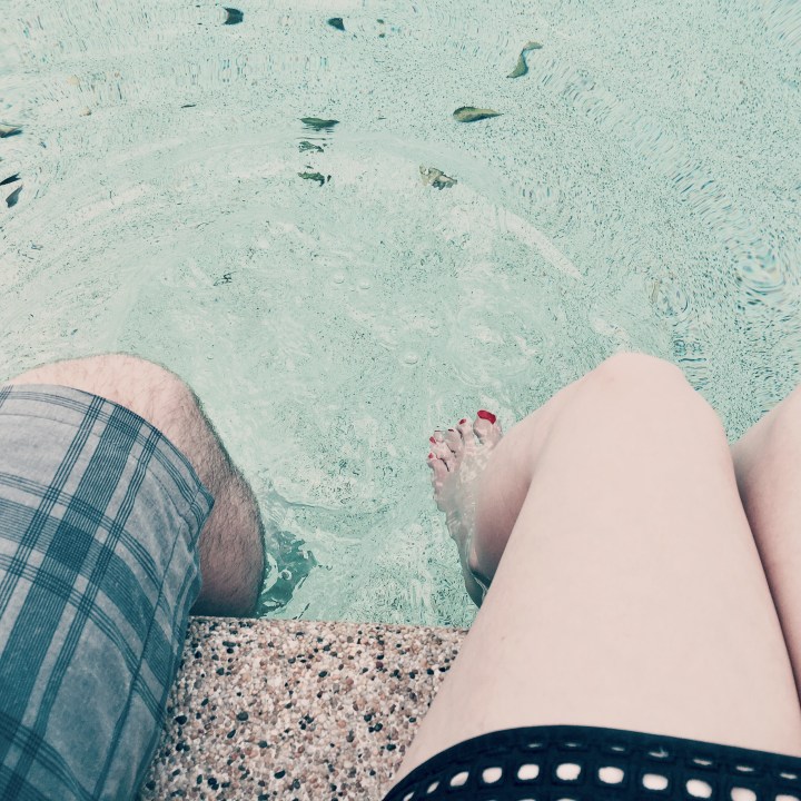 Man and woman's legs dangling in a pool.