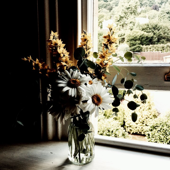 Bunch of yellow and white flowers sitting on a window sill.