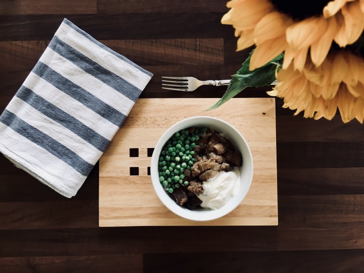 Beef stronganoff in a bowl, surrounded by a blue and white stripe napkin and a bunch of sunflowers.
