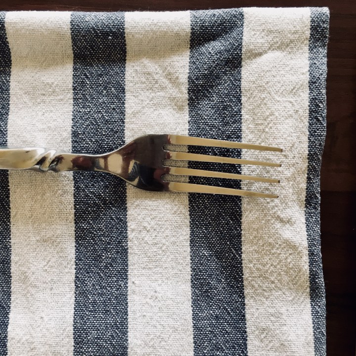 Fork sittting atop a blue and white striped linen napkin.