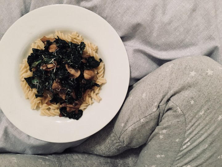 Pasta with mushrooms and cavolo nero sitting beside legs in pyjamas.
