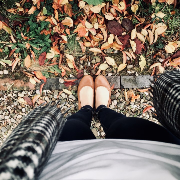 Looking down on a pair of legs wearing dark wash jeans and tan ballet flats surrounded by autumn leaves.