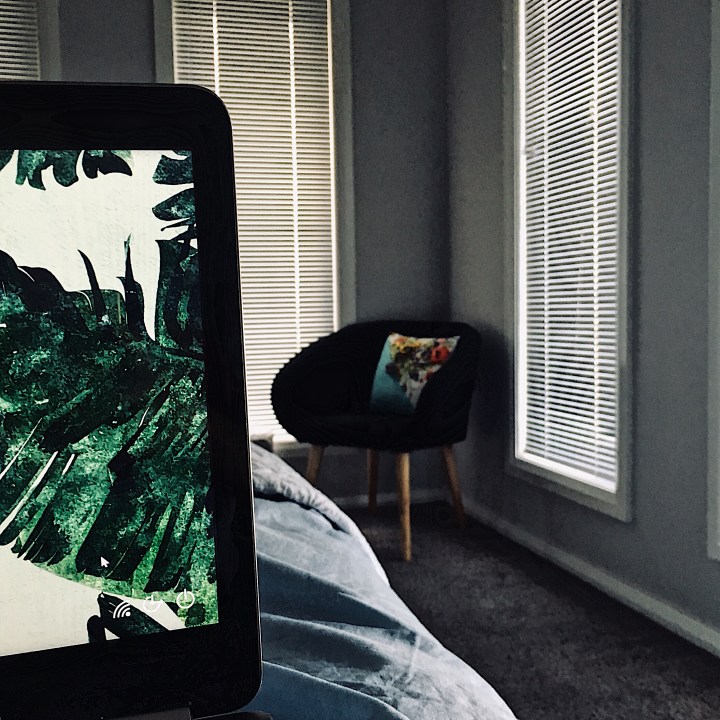 Person in bed looking at laptop computer and occasional chair in corner.