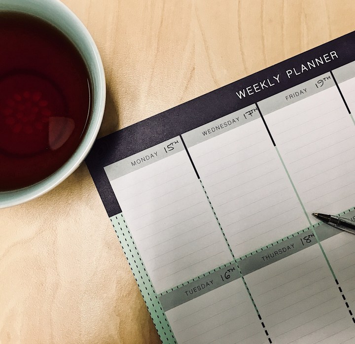 Mug of black tea and weekly planner on desk.