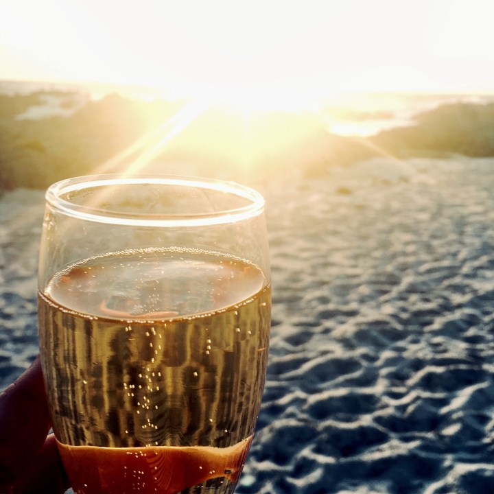Glass of champagne on the beach at sunset.
