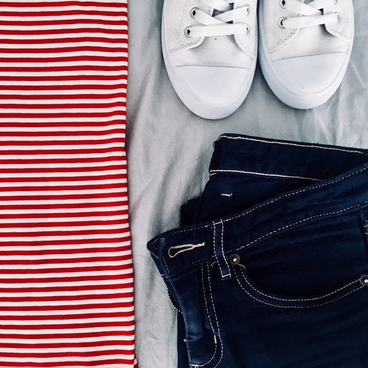 Flat lay of dark blue jeans, red and white stripe shirt and white sneakers.
