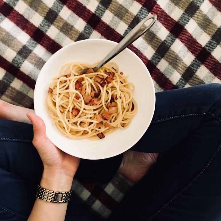 Hand holding bowl of pasta on check wool blanket