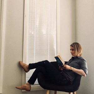 Woman reading wearing dark chambray shirt, dark blue jeans and nude loafers.