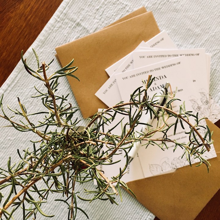 Wedding invitations, envelopes and a vase of rosemary.
