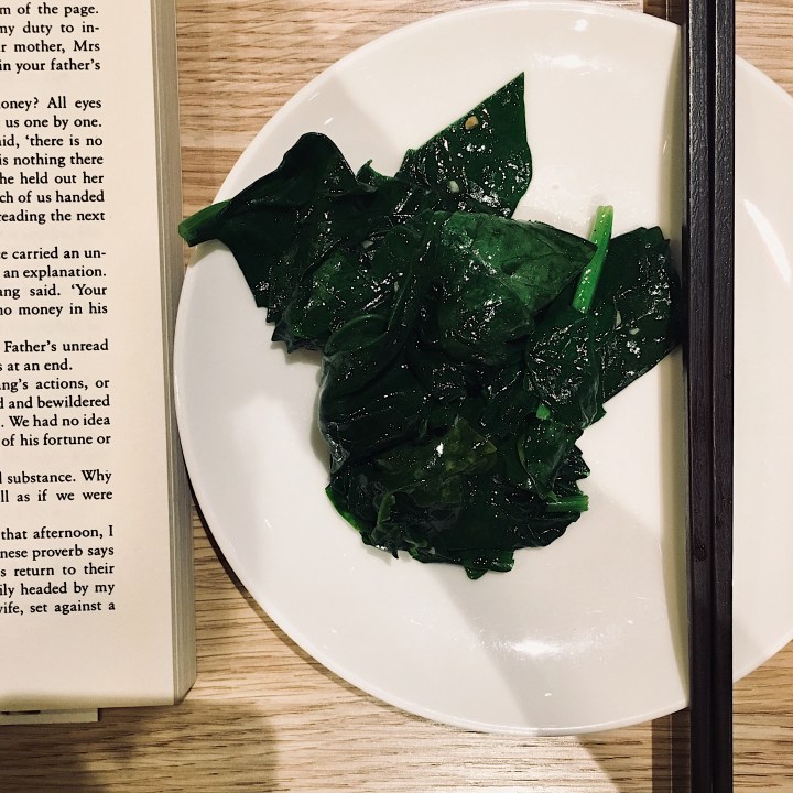 Book, plate of sauteed spinach and chopsticks.