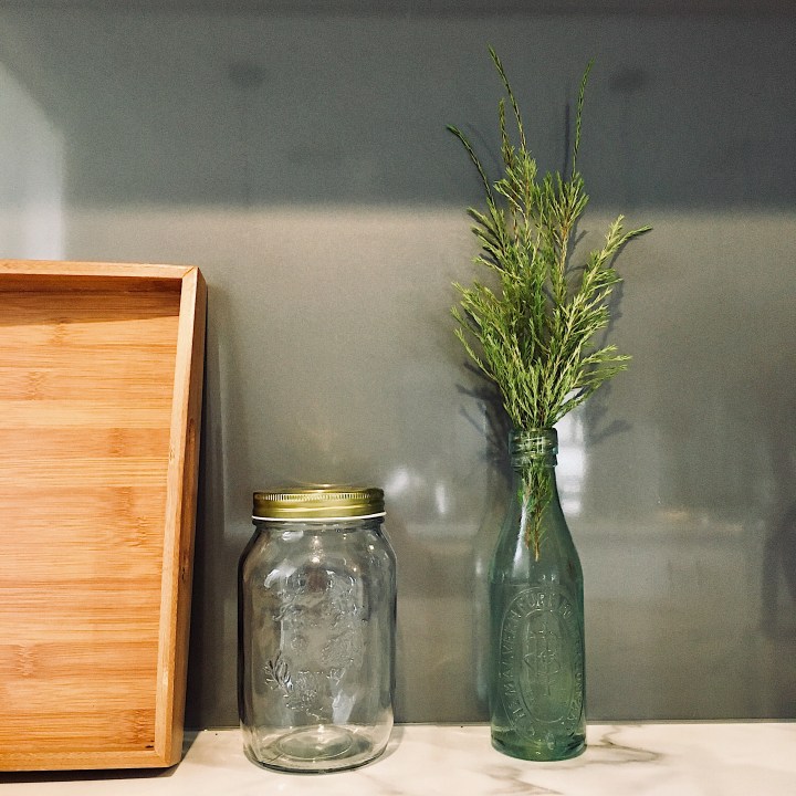 Greenery displayed in a bottle on a kitchen bench top.