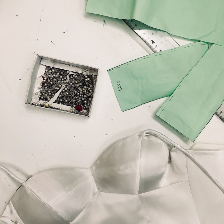 A silk-satin bustier, a wedding dress pattern and a box of pins sitting on a sewing table.