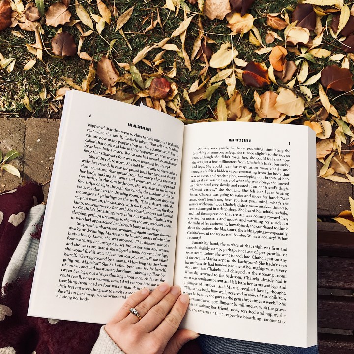 Woman reading on park bench surrounded by autumnal leaves.