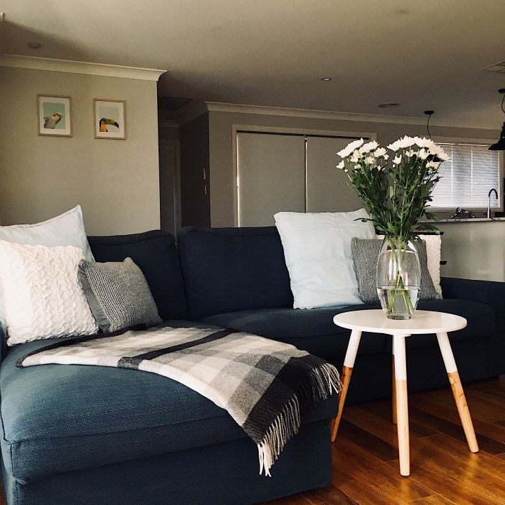 Dark blue lounge, style with blue, grey and white cushions, a black and white throw rug and Scandi inspired lamp table.