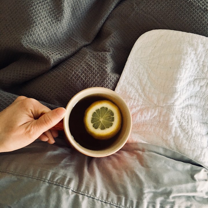 Woman in bed drinking a cup of tea with a slice of lemon.