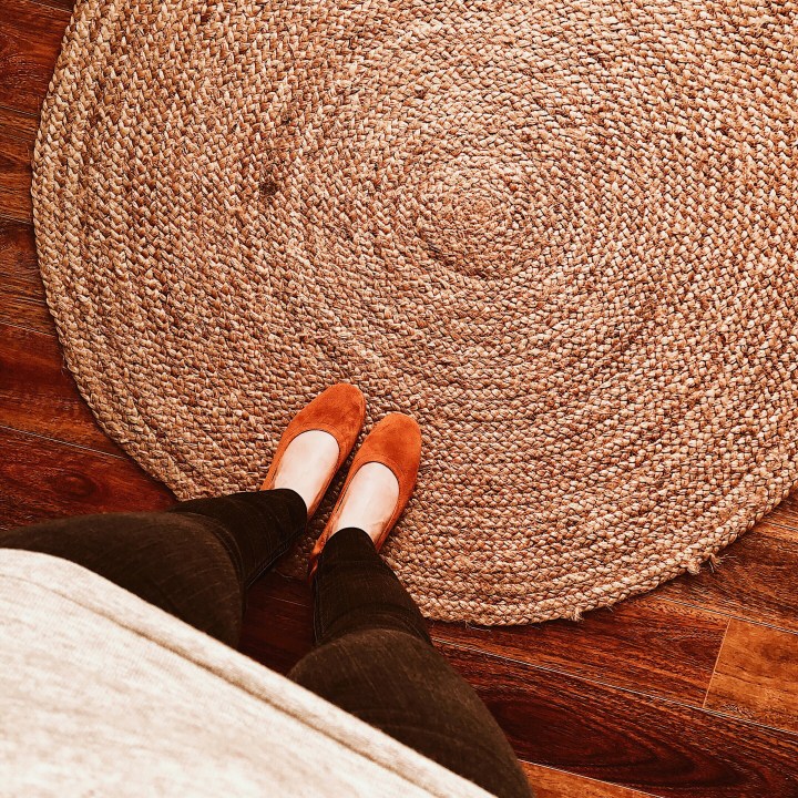 Woman standing in cognac Everlane day heels on jute rug.