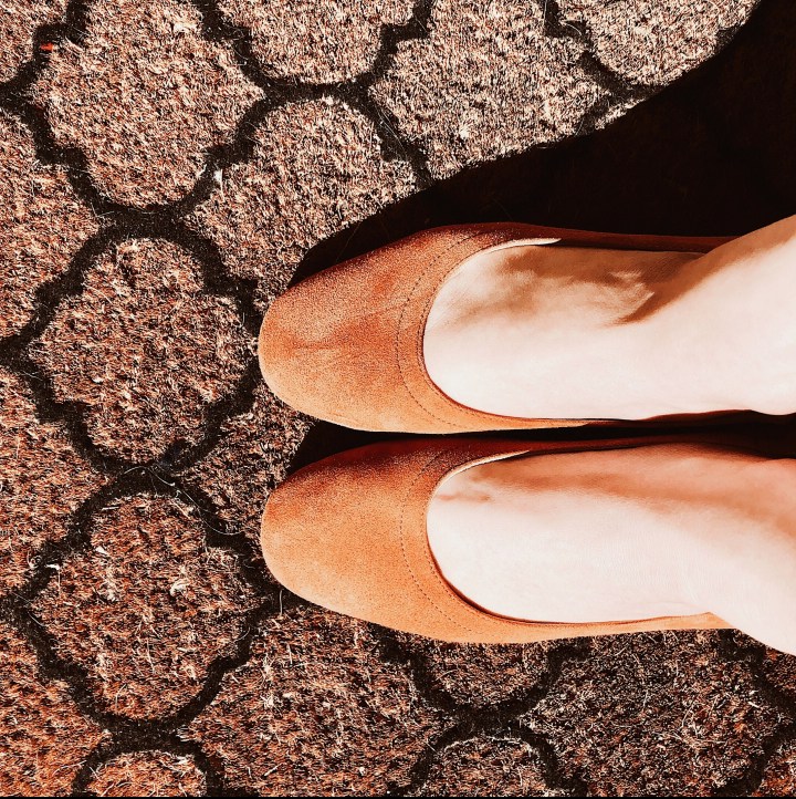 Woman standing in cognac Everlane day heels on patterned door mat.