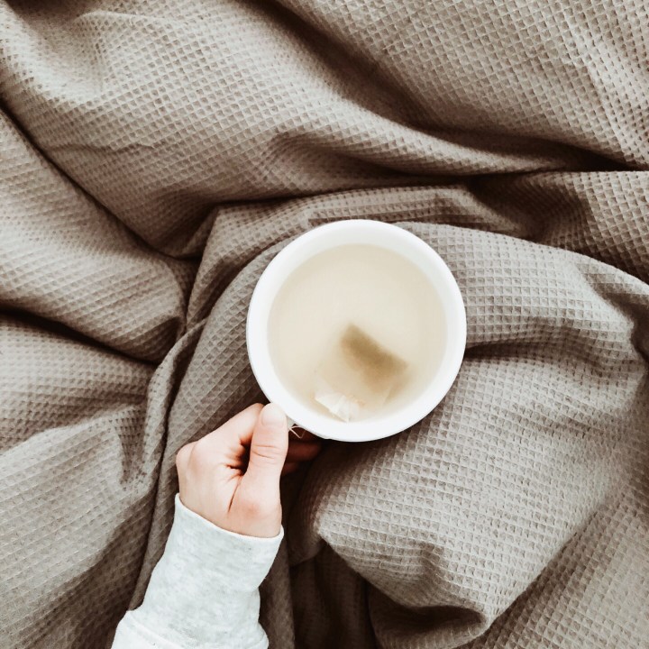 Woman holding a cup of tea of a grey duvet.