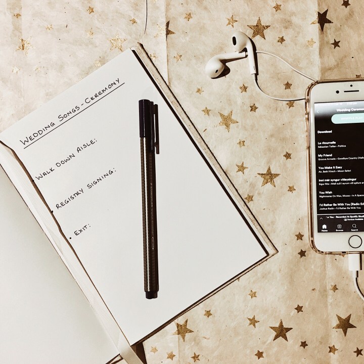 Phone, headphones and notepad sitting on cream and gold background.