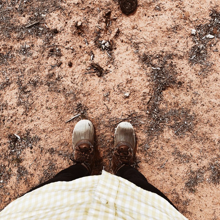 Looking down on a pair of dusty boots on bare earth.