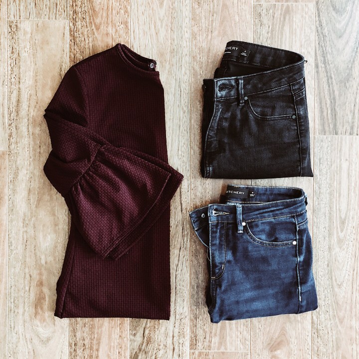 Flat lay of burgundy frill sleeve dress, dark blue jeans, black jeans.
