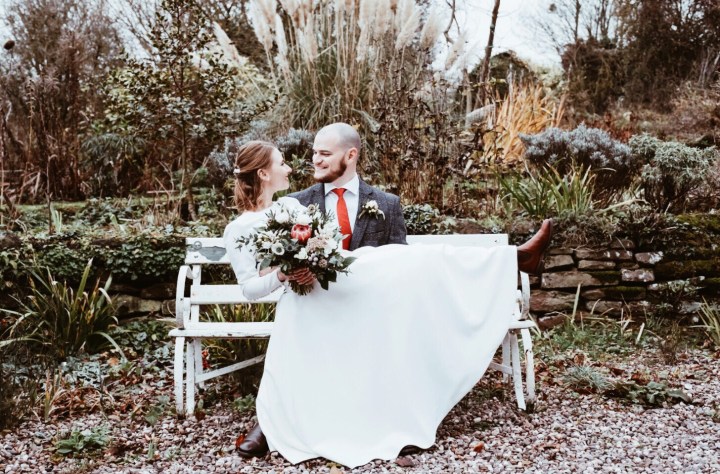 Bride holding bouquet sitting on groom's knee.