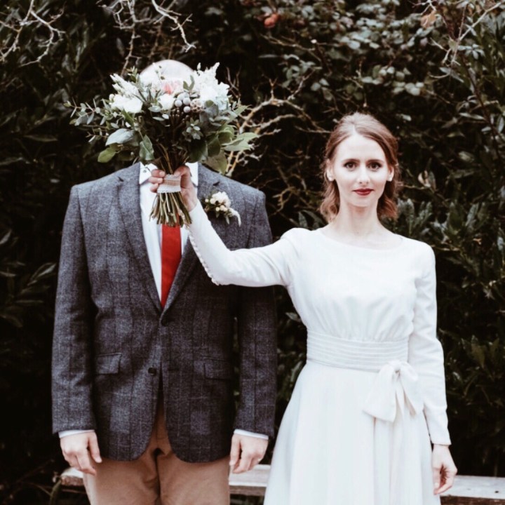Bride holding bouquet of flowers in front of groom's face.