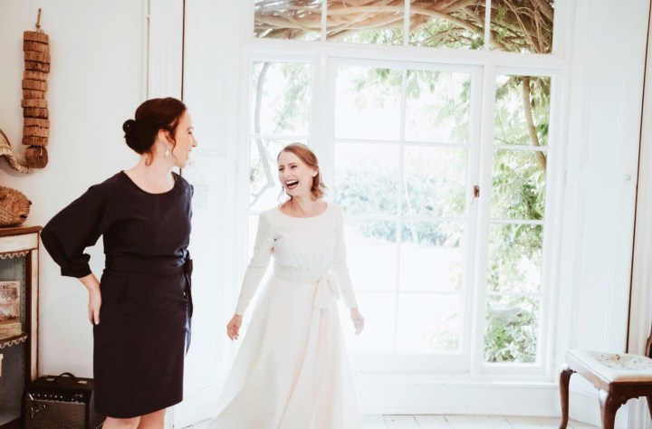 Bride and bridesmaid laughing in front of a window.