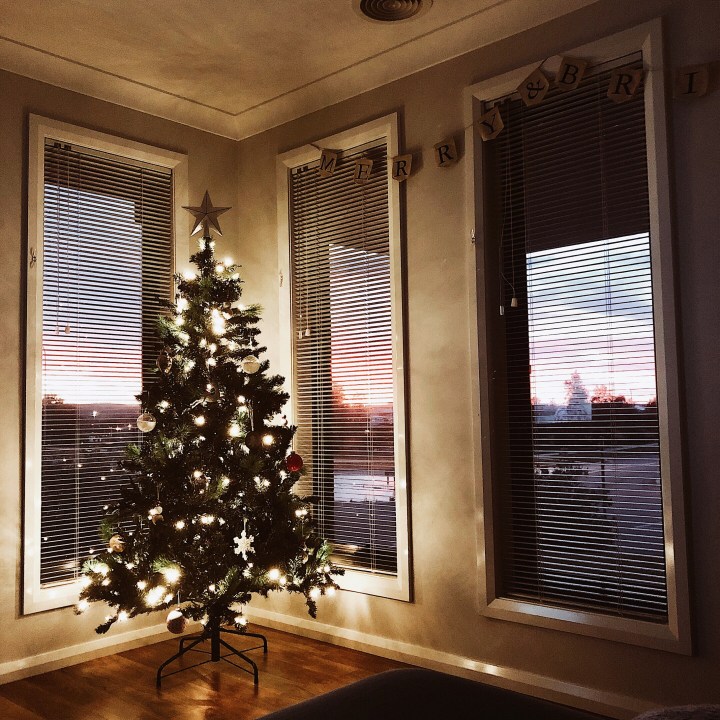 Lit Christmas tree standing in the corner of a room.