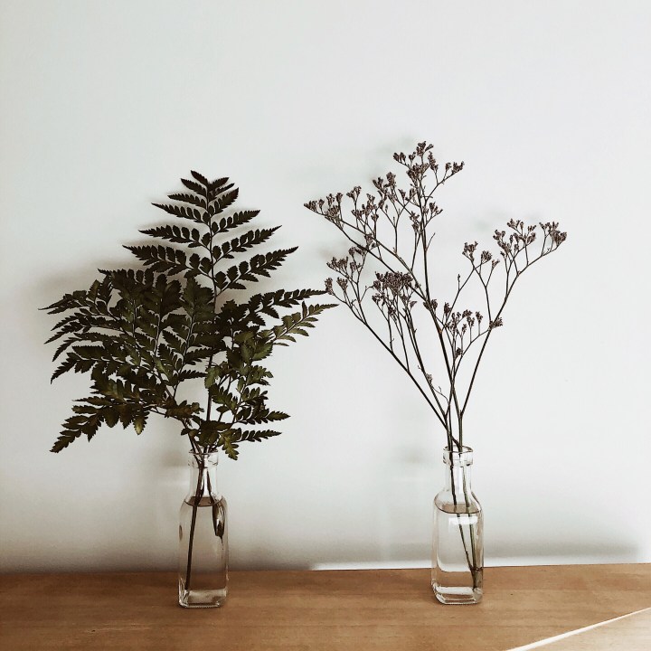 Wildflowers and fern leaves sitting in small bottles on an oak look bench.