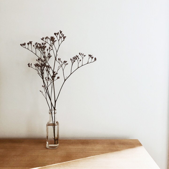 Wildflowers in a small bottle sitting on an oak look bench.