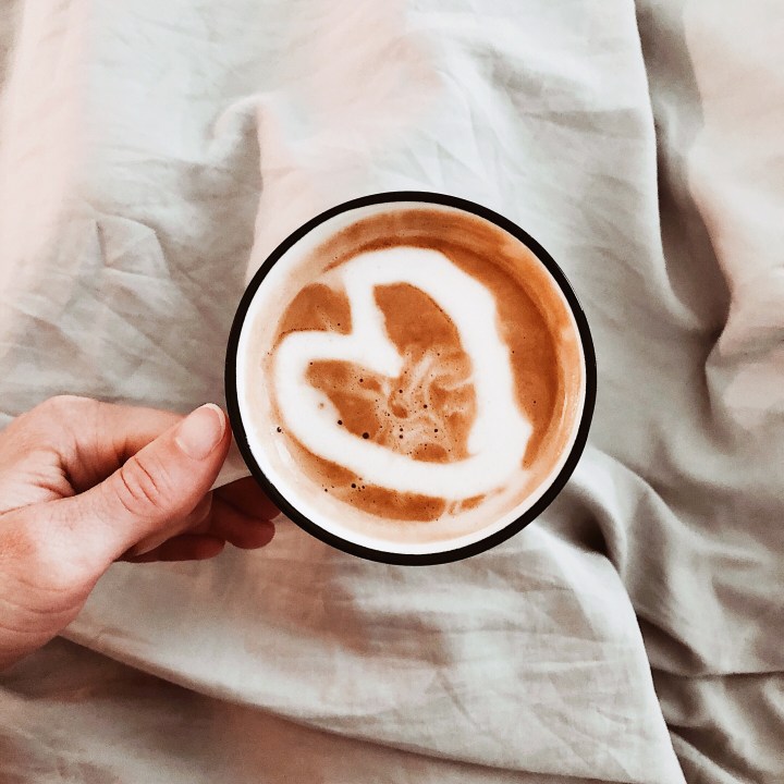 Hand holding coffee mug with heart drawn in it.