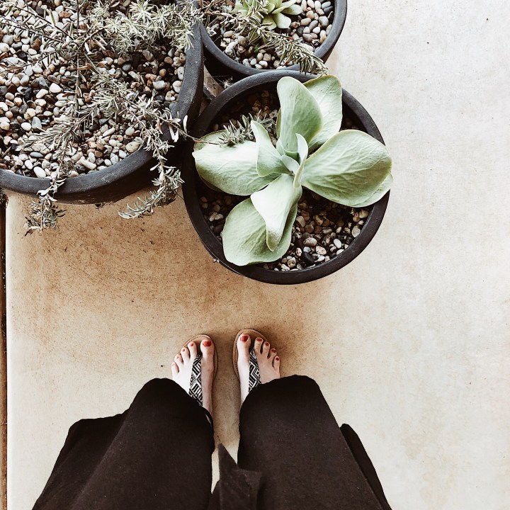Looking down at woman wearing wide legged linen trousers, standing near pots of succulents.