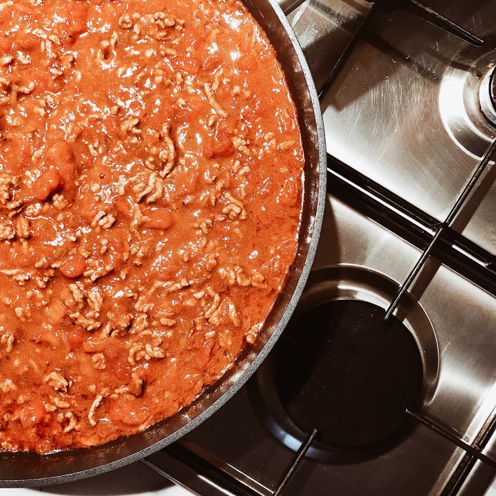 Red onions frying in a pan, with diced garlic on a chopping board besides.