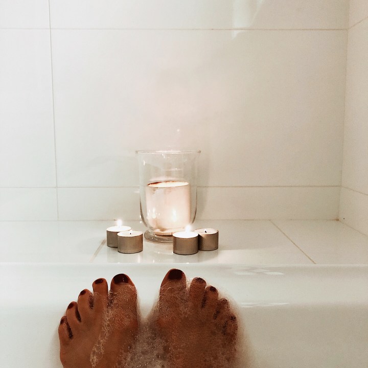 Feet in a bubble bath, looking onto a collection of candles.
