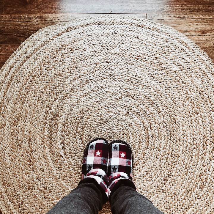 Looking down at a woman wearing slippers on a jute rug.