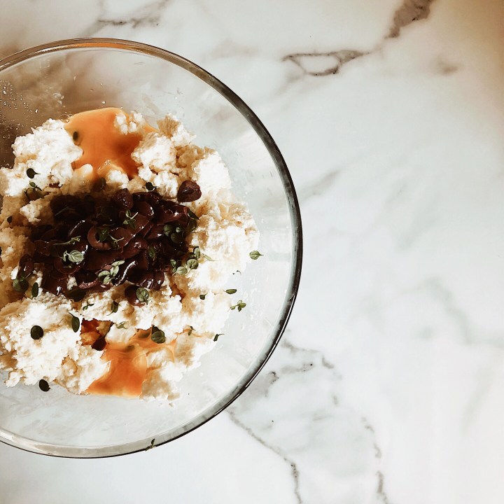 Ingredients for baked ricotta with olives, sitting in a glass mixing bowl.