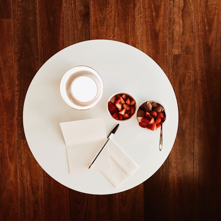 Looking down at a candle, card and pen, a bowl of chocolate mousse and a bowl of strawberries.
