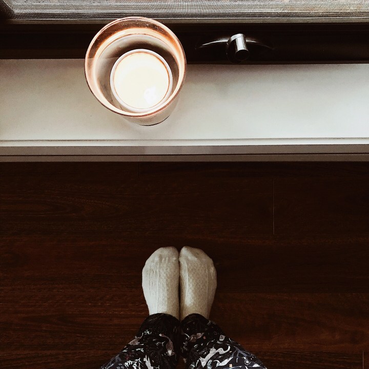 Looking down at a pair of feet in white cashmere socks and a candle sitting on a window-sill.