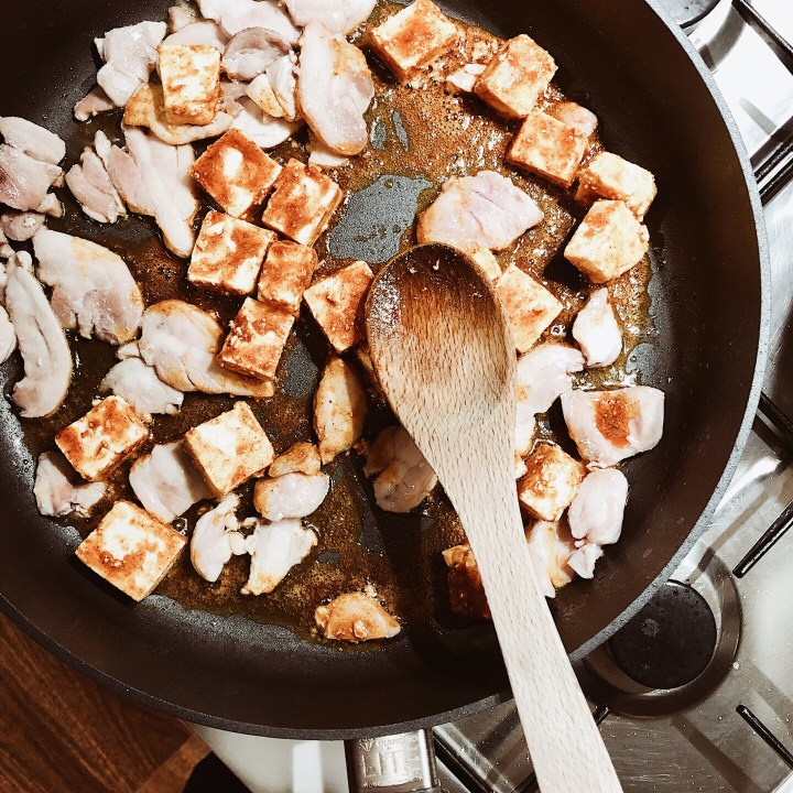 Chicken thigh and paneer cooking in a frypan.